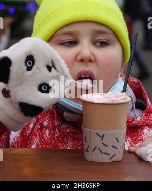 Une petite fille heureuse boit du chocolat chaud avec un guimauve sucré à l'extérieur. Banque D'Images