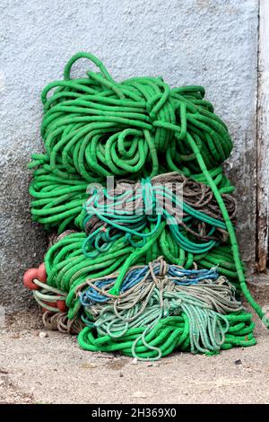 Grande pile de multicouleurs fortement utilisé de vieux cordages navals épais mélangés avec de petites bouées rouges laissées à côté de la maison en ruine mur sur route de gravier sur chaud Banque D'Images