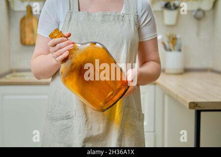 Une femme tient un grand vase en bouteille dans ses mains tout en se tenant sur une cuisine maison, gros plan Banque D'Images