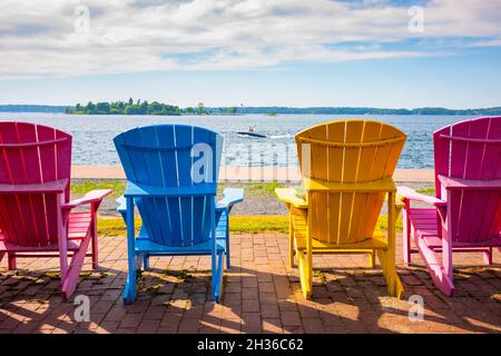 Quatre chaises Adirondack peintes alignées le long de la rive du fleuve Saint-Laurent à Clayton, New York. Banque D'Images