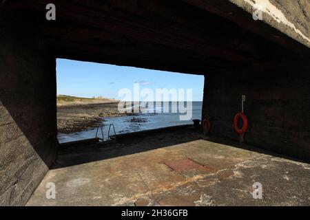 Le château de Dunstanburgh, datant du XIVe siècle, au nord de Craster, à Northumberland, au Royaume-Uni, vu du port de Craster. Banque D'Images