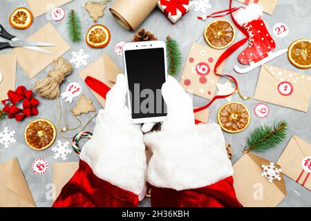 Mains du Père Noël avec un téléphone.Préparation du calendrier de l'Avent.Tradition de Noël saisonnière.Flat lay, vue de dessus. Banque D'Images