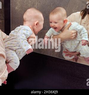 Un bébé heureux dans les bras de sa mère s'est vu dans le miroir et rit Banque D'Images