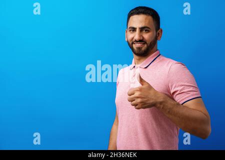 Bonne barbe jeune homme souriant avec les pouces vers le haut sur fond bleu Banque D'Images