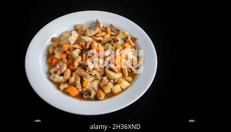 Un plat chinois traditionnel de ragoût de poulet, avec des amandes, des carottes et des pâtes.Dans une plaque sur fond noir, gros plan. Banque D'Images