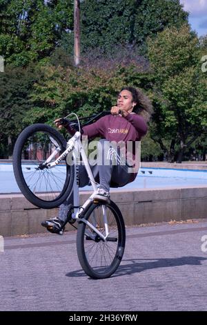 Un jeune homme aux cheveux longs fait des roues sur son vélo tout en faisant des tours dans le Unisphere à Flushing Meadows Corona Park à Queens, New York. Banque D'Images