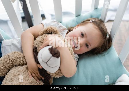 Vue de dessus de bébé fille avec le syndrome de Down embrassant le jouet doux dans le berceau Banque D'Images