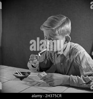 Série: Ein neugieriger Junge probiert seine erste Zigarette, Deutschland 1940er Jahre.Un curieux garçon essayant sa première cigarette, Allemagne des années 1940. Banque D'Images