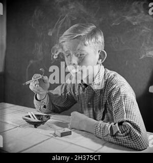 Série: Ein neugieriger Junge probiert seine erste Zigarette, Deutschland 1940er Jahre.Un curieux garçon essayant sa première cigarette, Allemagne des années 1940. Banque D'Images