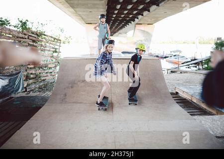 Garçons filles amis ont le plaisir ensemble hurler pendant l'entraînement de skateboard, de l'équitation et de faire des tours sur demi-pipe dans le parc de skate.Jeunes, ensemble et Banque D'Images