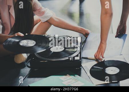 Les jeunes femmes s'assoient sur le sol et explorent les disques vinyles, les mettent sur un joueur rétro. Banque D'Images