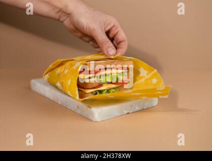 Un sandwich traditionnel composé de tranches de pain grillées, de fromage, de jambon, de salade fraîche enveloppée de papier bio réutilisable à base de cire d'abeille.Célébration du Sandwi national Banque D'Images