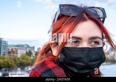 Anonyme jeune femme ou adolescente portant Un masque de protection contre le coronavirus Covid-19 avec London Skyline derrière elle Banque D'Images