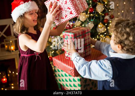 Les enfants adorés et heureux sourient, jouant avec une pile de cadeaux de Noël.Salon joliment décoré avec des lumières et un sapin de Noël. Banque D'Images