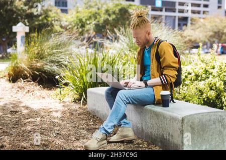 Albino réfléchi homme africain américain avec des dreadlocks assis dans le parc à l'aide d'un ordinateur portable Banque D'Images