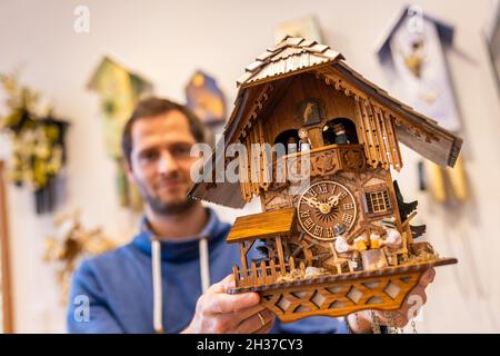 26 octobre 2021, Baden-Wuerttemberg, Schonach im Schwarzwald : Andreas Kreyer, directeur général de Rombach & Haas et membre de la Black Forest Clock Association, est debout dans la salle de vente de l'entreprise, avec une horloge à coucou de conception traditionnelle dans sa main tandis que des exemples modernes sont accrochés au mur derrière lui.La pandémie de Corona et ses conséquences complexes ont paralysé de nombreux métiers.Même les fabricants de cuckoo horloge dans la Forêt Noire en ressentent les effets.La production d'horloges à coucou en Allemagne s'est effondrée de plus de la moitié l'année dernière.Le dimanche soir (31 octobre), les horloges W Banque D'Images