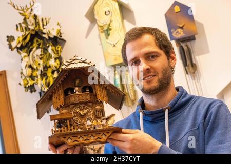 26 octobre 2021, Baden-Wuerttemberg, Schonach im Schwarzwald : Andreas Kreyer, directeur général de Rombach & Haas et membre de la Black Forest Clock Association, est debout dans la salle de vente de l'entreprise, avec une horloge à coucou de conception traditionnelle dans sa main tandis que des exemples modernes sont accrochés au mur derrière lui.La pandémie de Corona et ses conséquences complexes ont paralysé de nombreux métiers.Même les fabricants de cuckoo horloge dans la Forêt Noire en ressentent les effets.La production d'horloges à coucou en Allemagne s'est effondrée de plus de la moitié l'année dernière.Le dimanche soir (31 octobre), les horloges W Banque D'Images