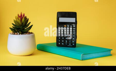 Calculatrice sur un carnet vert avec une fleur de cactus sur fond jaune. Banque D'Images