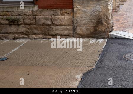 Coin d'un bâtiment en brique rouge et en pierre roustiquée qui rencontre un trottoir en brique, une allée en béton et une surface de route asphaltée, aspect horizontal Banque D'Images