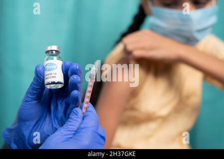 Maski, Inde - 26 octobre 2021 : accent sélectif sur la bouteille de vaccin - enfant avec masque médical se faisant vacciner Covid-19 ou coronavirus de Pfizer Banque D'Images