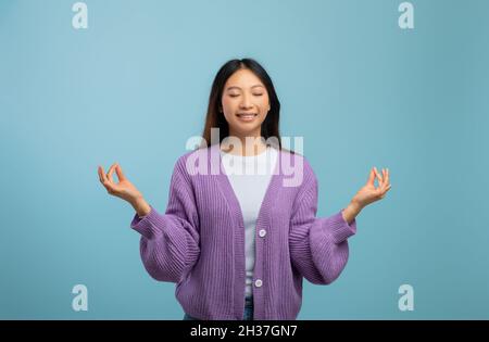 Zen.Femme asiatique paisible méditant avec les yeux fermés, pratiquant le yoga et gardant les mains dans le geste de mudra Banque D'Images