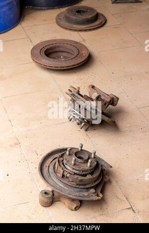 Moyeux arrière anciens, usagés et rouillés, sur lesquels les plaquettes de frein du frein de stationnement sont visibles, et disques de frein sur le sol carrelé beige de l'atelier de réparation automobile Banque D'Images