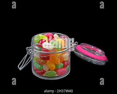 Ouvrez le pot en verre de jelly Beans coloré isolé sur fond noir Banque D'Images