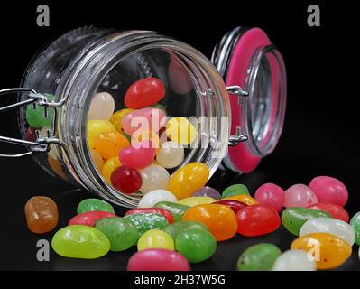 pot en verre de jelly haricots colorés renversé sur fond noir Banque D'Images