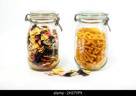 Deux types de pâtes brutes dans des pots en verre fermés isolés sur fond blanc.Pâtes italiennes gros plan : fusilli et farfalle Banque D'Images