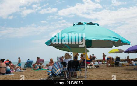 VALENCE, ESPAGNE - 22 septembre 2021 : Alcossebre, Espagne - août 2021.Plage de mer bondée avec des touristes qui bronzer devant un parasol bleu. Banque D'Images