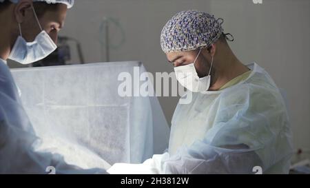 Détails d'une véritable chirurgie dans le bloc opératoire stérile.Action.Antécédents médicaux des médecins portant un uniforme stérile et un masque facial au travail au Banque D'Images