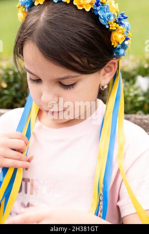 Fille triste avec décoration folklorique ukrainienne sur sa tête.Petit enfant touchant les rubans de couronne en se tenant debout à l'extérieur Banque D'Images