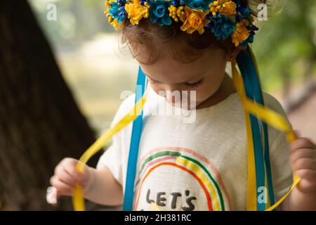 Fille triste avec décoration folklorique ukrainienne sur sa tête.Petit enfant touchant les rubans de couronne en se tenant debout à l'extérieur Banque D'Images