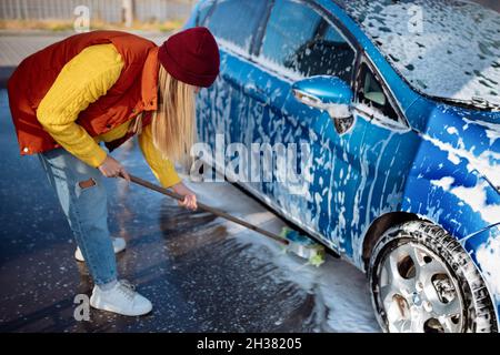 Belle jeune fille lave la voiture au lavage de voiture libre-service. Effacer la saleté à la voiture avec une brosse Banque D'Images