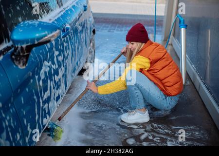 Belle jeune fille lave la voiture au lavage de voiture libre-service. Effacer la saleté à la voiture avec une brosse Banque D'Images