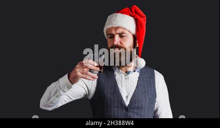 Dégustation Whiskey.Boissons scotch ou cognac.Sommelier.Homme barbu dans un chapeau de Noël avec un verre de whisky ou de Brandy. Banque D'Images