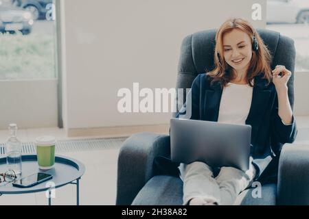 Heureuse redhead femme freelance dans le micro-casque communiquant avec le client pendant les appels vidéo sur ordinateur portable Banque D'Images