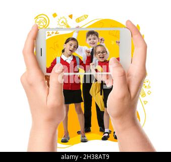 Femme avec téléphone mobile prenant des photos de petits écoliers sur fond blanc Banque D'Images