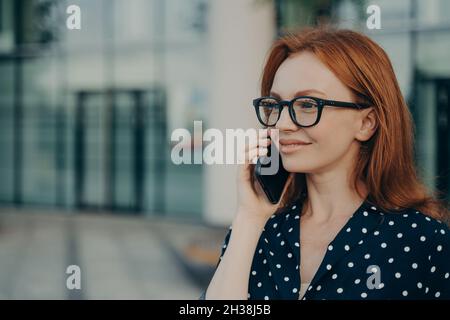 REDHEAD femme d'affaires a la conversation téléphonique utilise un gadget cellulaire moderne Banque D'Images