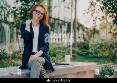 Frustrée tête rouge la jeune femme se sent très fatiguée souffre de douleurs au cou assis dans le parc Banque D'Images