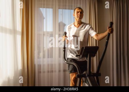 Un homme dans un T-shirt blanc court sur un ellipsoïde à la maison Banque D'Images