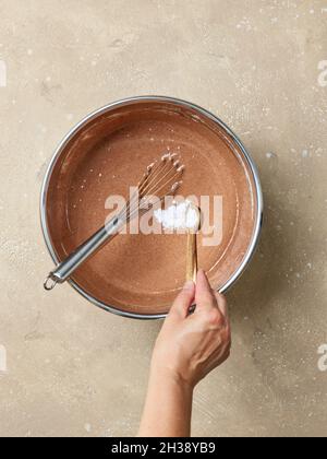 ajout de bicarbonate de soude dans un bol de pâte à gâteau au chocolat, vue du dessus Banque D'Images