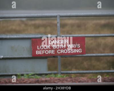 Panneau d'avertissement indiquant « danger, regardez dans les deux sens avant de traverser » sur une clôture en métal Banque D'Images