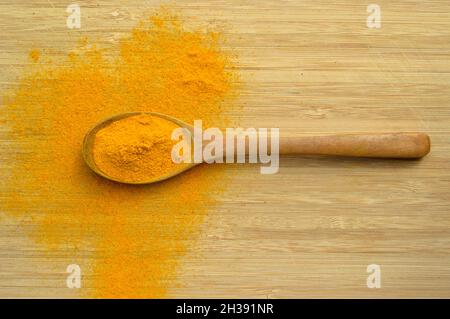 Curcuma frais en poudre aromatique dans une cuillère en bois sur fond en bois de bambou Banque D'Images