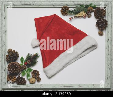 Chapeau de père noël rouge dans un cadre en bois de merde sur fond blanc avec des branches de sapin et des cônes dans les coins Banque D'Images