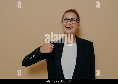 Portrait d'une femme satisfaite en lunettes souriant tout en montrant le pouce vers le haut avec la main Banque D'Images