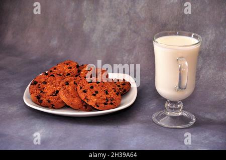 Une assiette avec plusieurs biscuits de flocons d'avoine au chocolat et un verre de lait sur un fond gris isolé.Gros plan. Banque D'Images