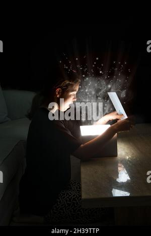 Jeune fille avant l'adolescence 11 12 13 ouvrant une boîte cadeau magique surprise lumineuse avec de la fumée lumineuse et de la musique Banque D'Images