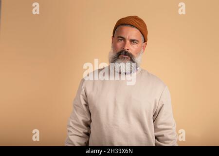 Portrait d'un bel homme barbu regardant sérieusement l'appareil photo sur fond beige. Banque D'Images
