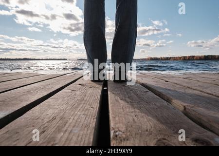 Une femme dans un Red Jacket est assise à une table sur un quai en bois et regarde l'eau, les nuages et les arbres avec le feuillage jaune.Paysage d'automne. Banque D'Images